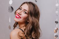close-portrait-attractive-girl-with-bright-lips-gray-eyed-curly-brown-haired-woman-cute-smiling-posing-gray-wall-with-sparkles